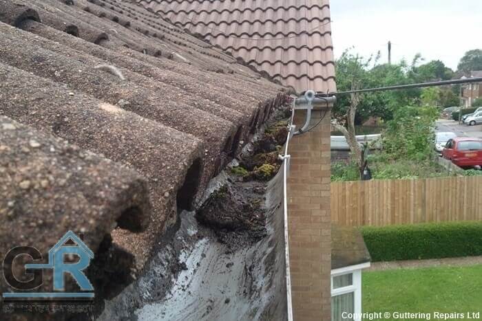Roof gutter repair and cleaning on a terraced house roof.