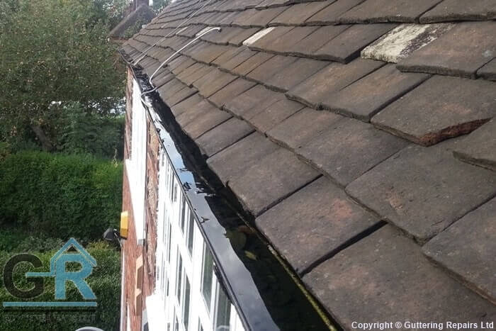Cast iron roof gutters on a residential property clogged with leaves and debris.